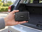 Hand holding a petZeye GPS 915 tracker beside an open vehicle boot
